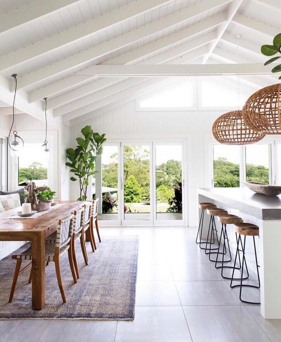 a dining room with white walls and wooden tables in the foreground is an open floor plan