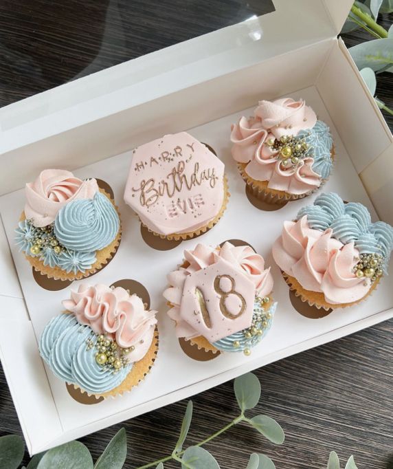 cupcakes with pink and blue frosting in a white box on a table