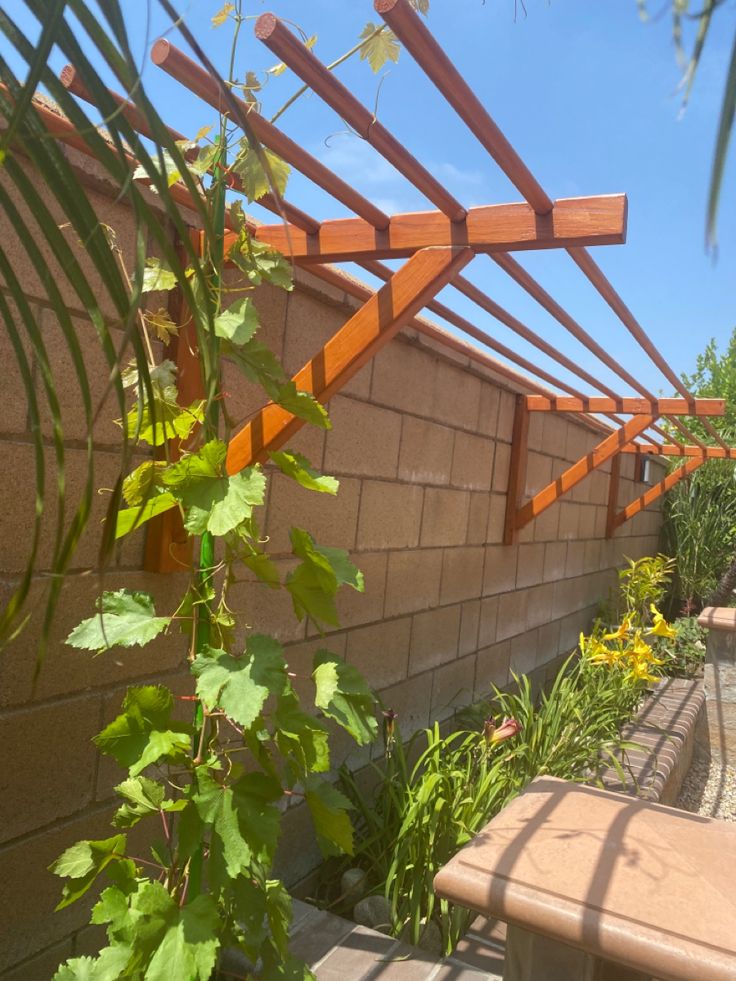 a wooden bench sitting next to a brick wall and green plants on the side of it