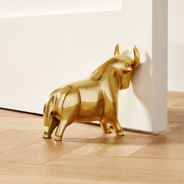 a gold bull figurine sitting on top of a wooden floor next to a white wall