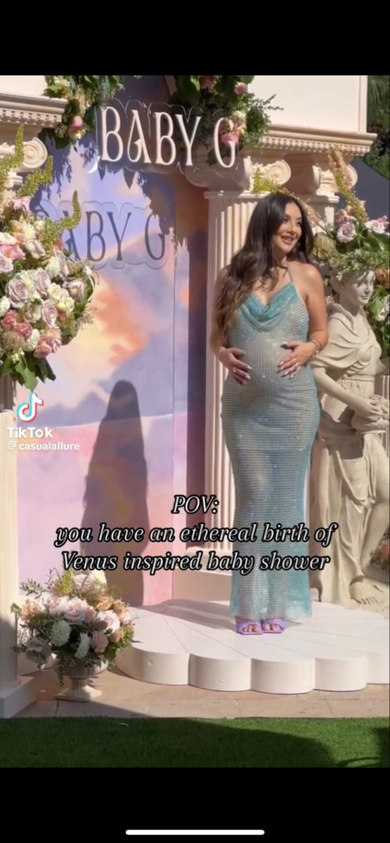 the pregnant woman is standing on stage in front of an arch with flowers and greenery