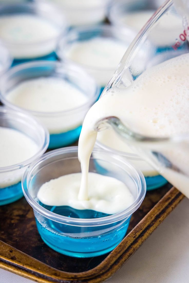 someone pouring milk into small cups on a tray