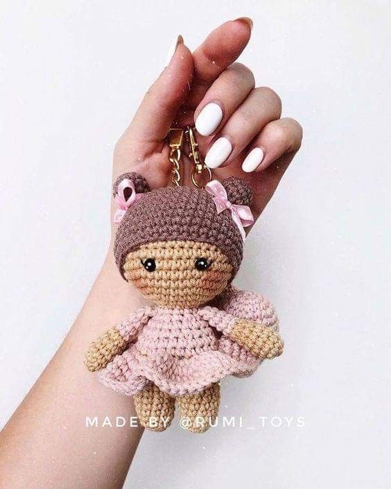 a hand holding a small crocheted doll in it's right arm and wearing a pink dress