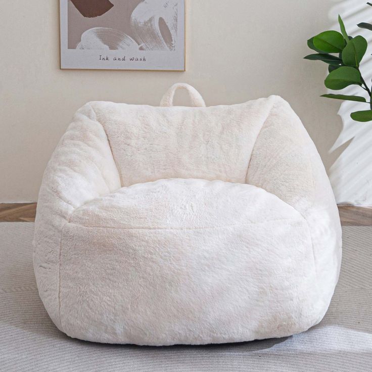 a white bean bag chair sitting on top of a wooden floor next to a potted plant