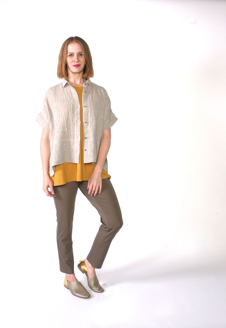 a woman standing in front of a white background wearing brown pants and a yellow shirt