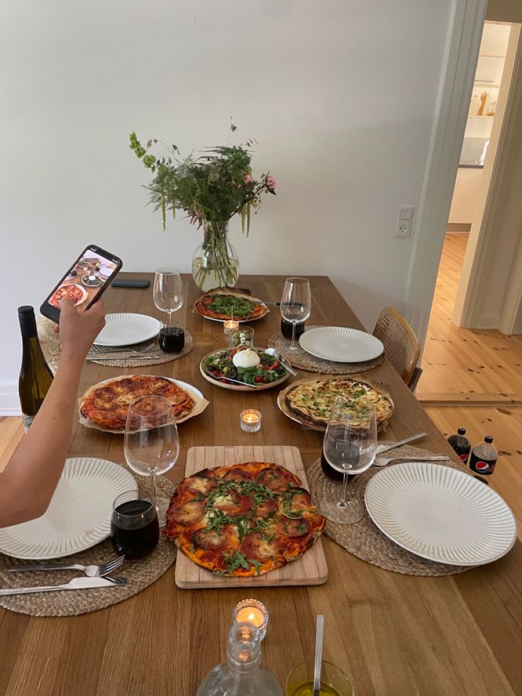 a person sitting at a table with pizza and wine in front of them on their cell phones