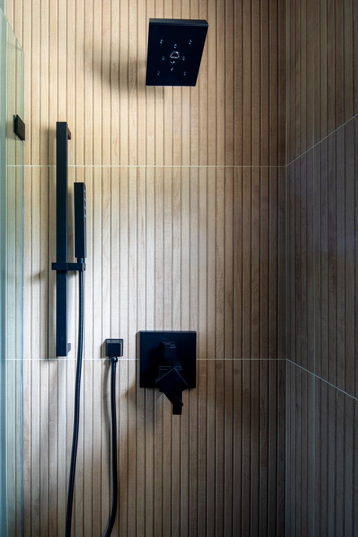 a shower head and hand shower in a bathroom with wood paneling on the walls