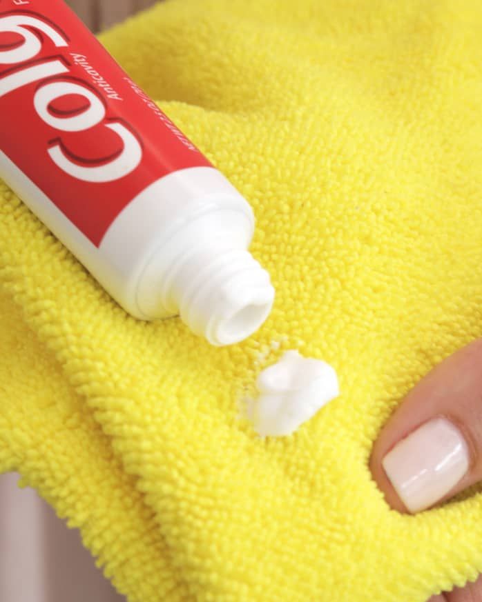 a hand holding a yellow towel with a tube of toothpaste on top of it