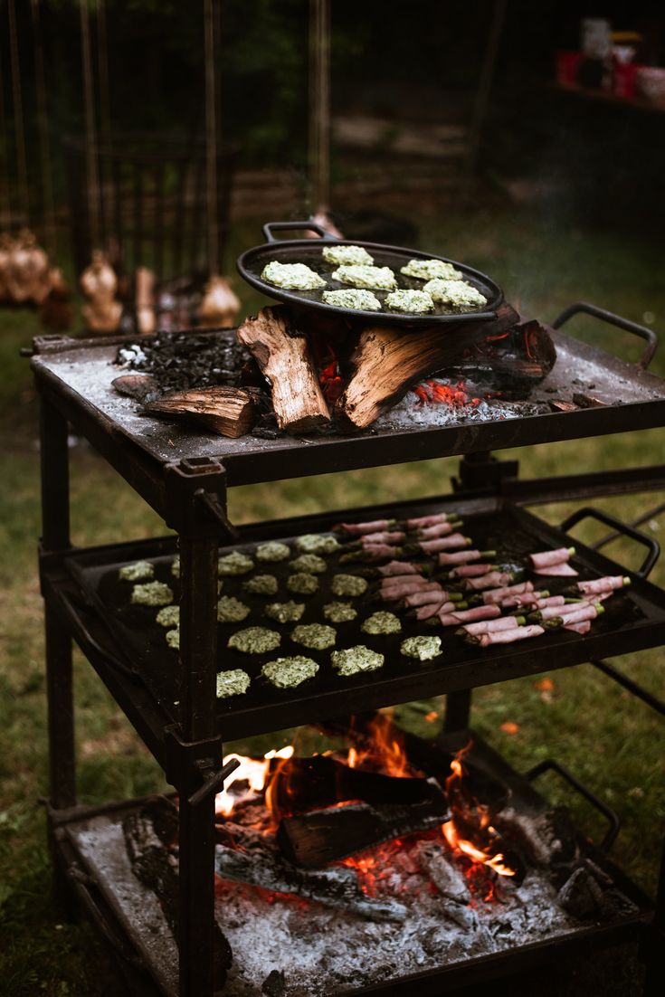 an outdoor grill with food cooking on it in the evening hours, and fire burning