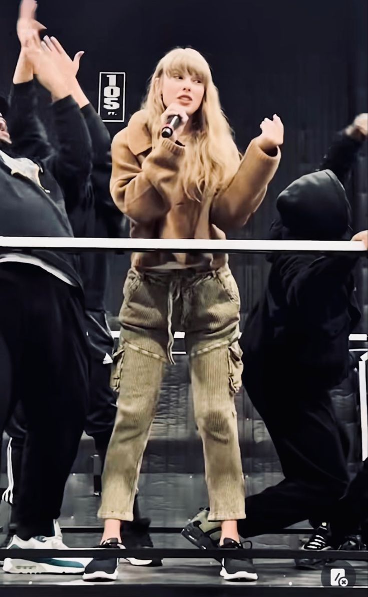 a woman standing on top of a stage with her hands in the air and other people behind her