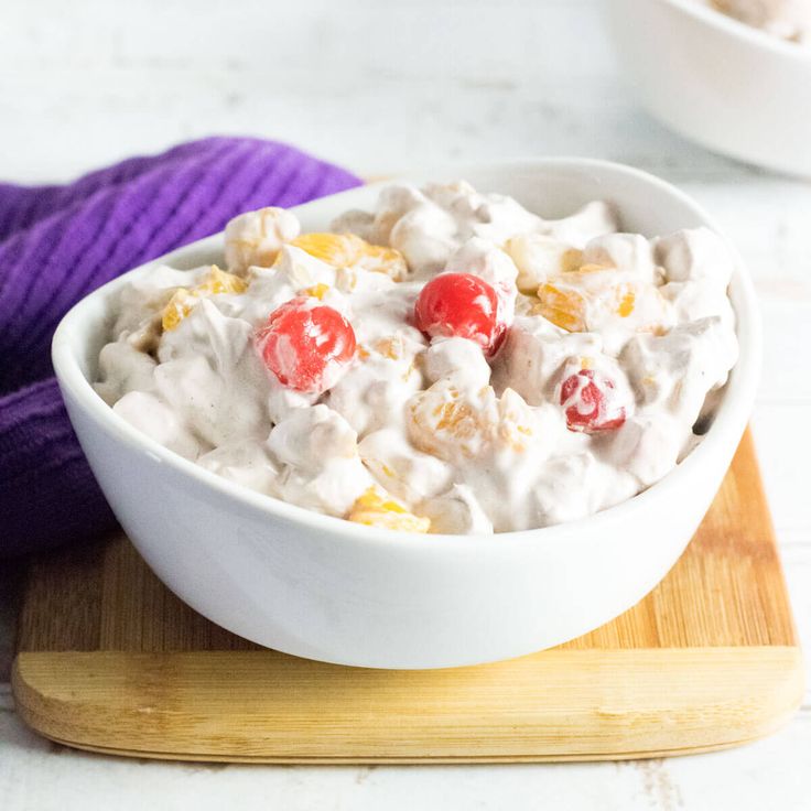 a white bowl filled with fruit salad on top of a wooden cutting board next to a purple towel