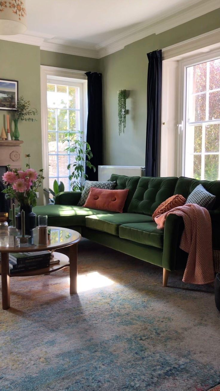 a living room with green couches and pink flowers in vases on the coffee table