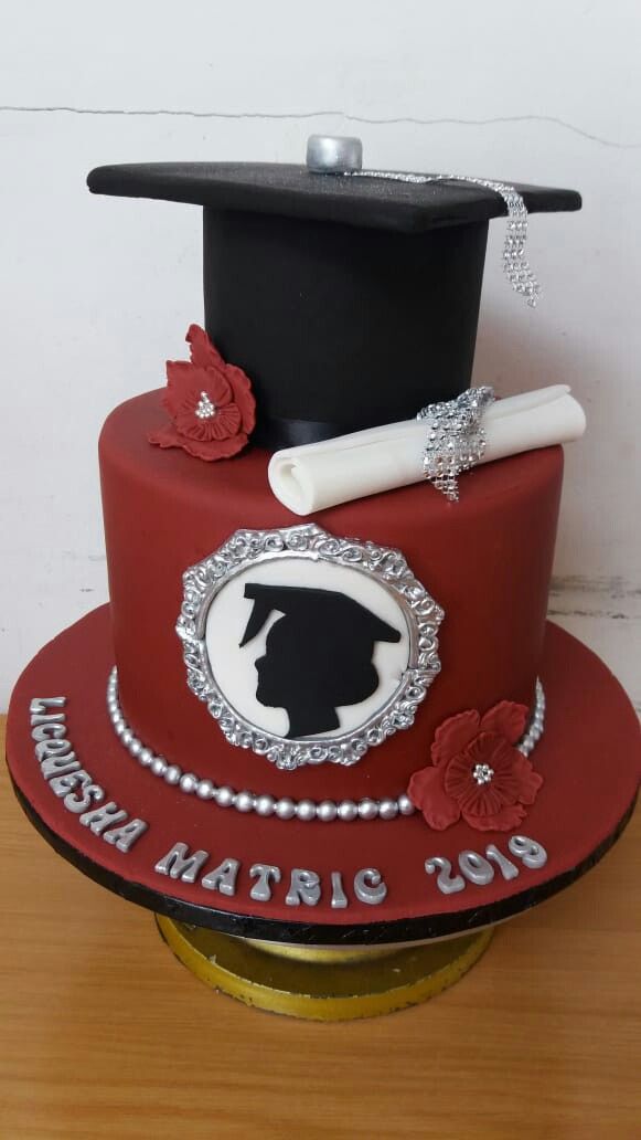 a red graduation cake with a mortar and diploma on top, sitting on a wooden table