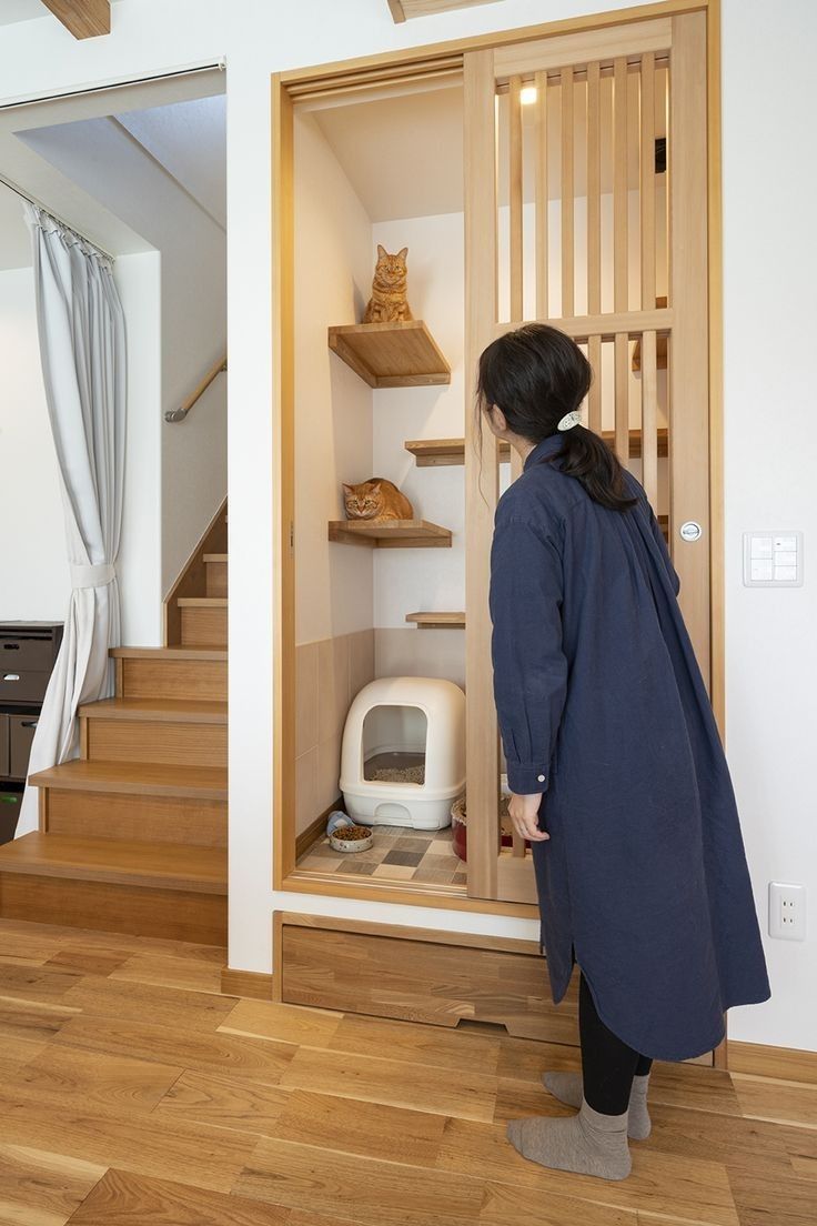 a woman standing in front of an open door with shelves on each side and a cat litter box behind her