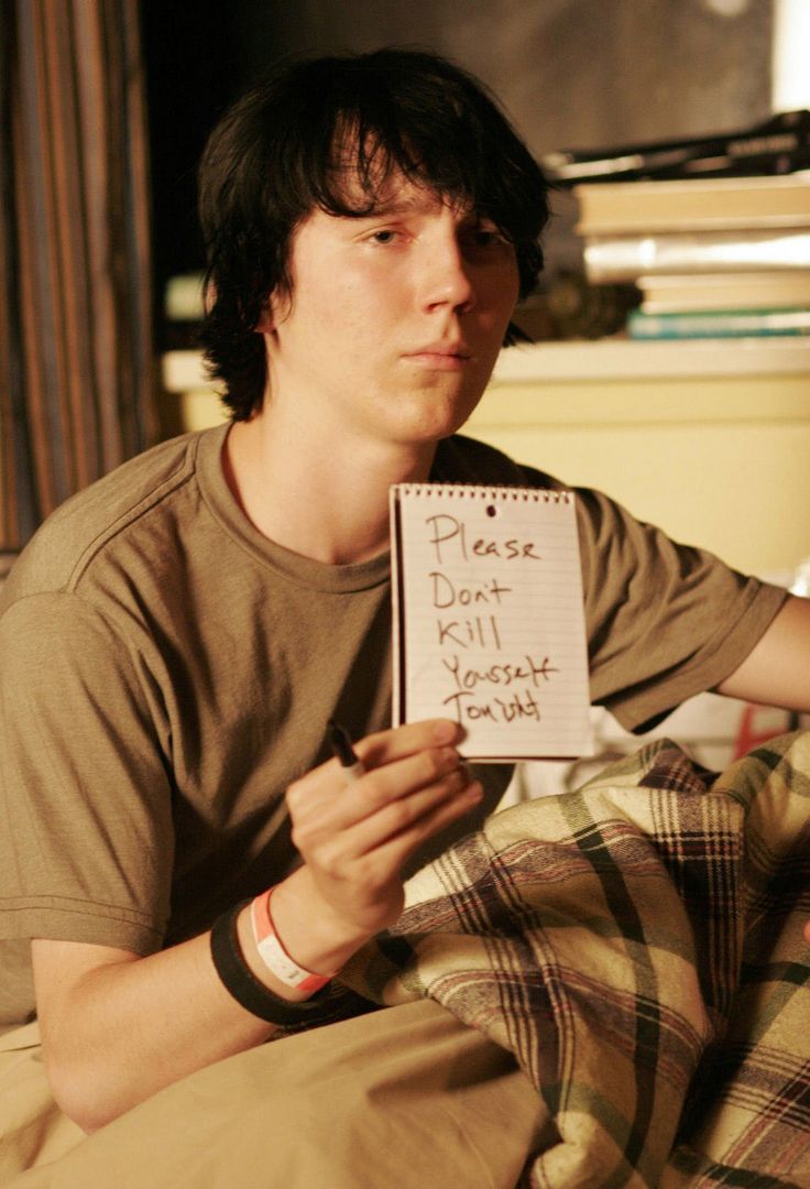 a young man sitting on top of a bed holding a note