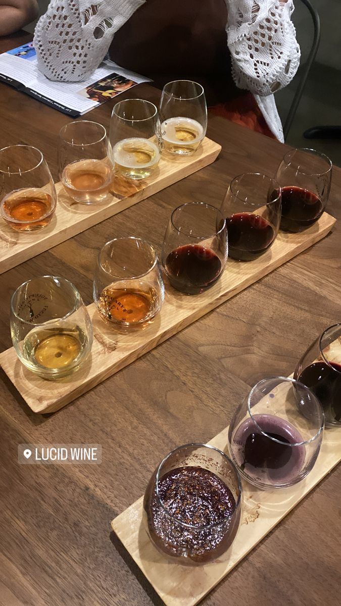 several glasses of wine sitting on top of a wooden tray next to another glass filled with liquid