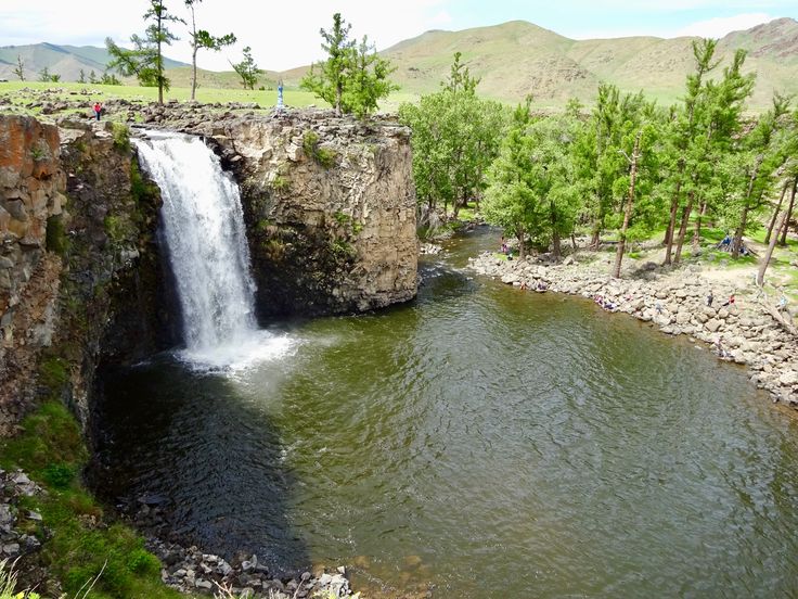 a small waterfall is coming out of the side of a rock wall into a river