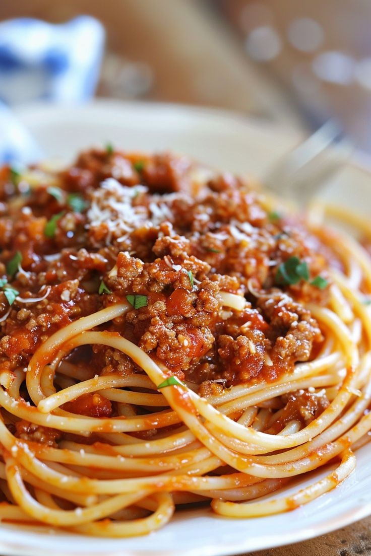 a plate of spaghetti with meat sauce and parmesan cheese on top, ready to be eaten