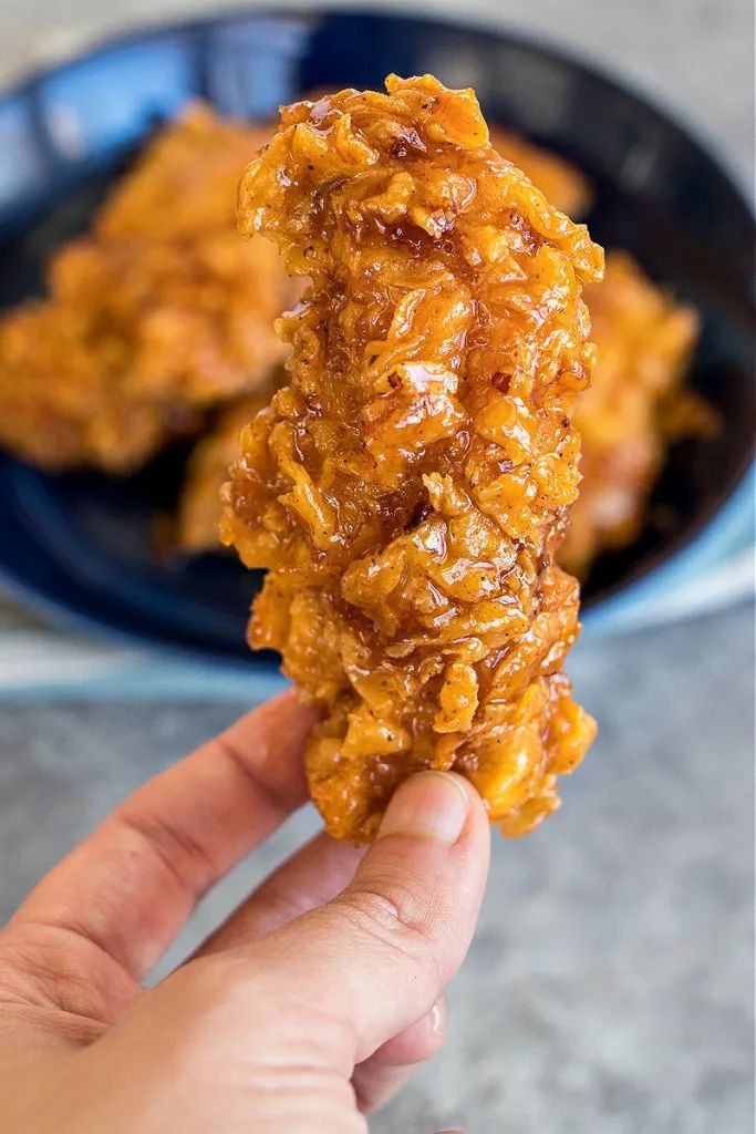 a hand holding up some food in front of a plate