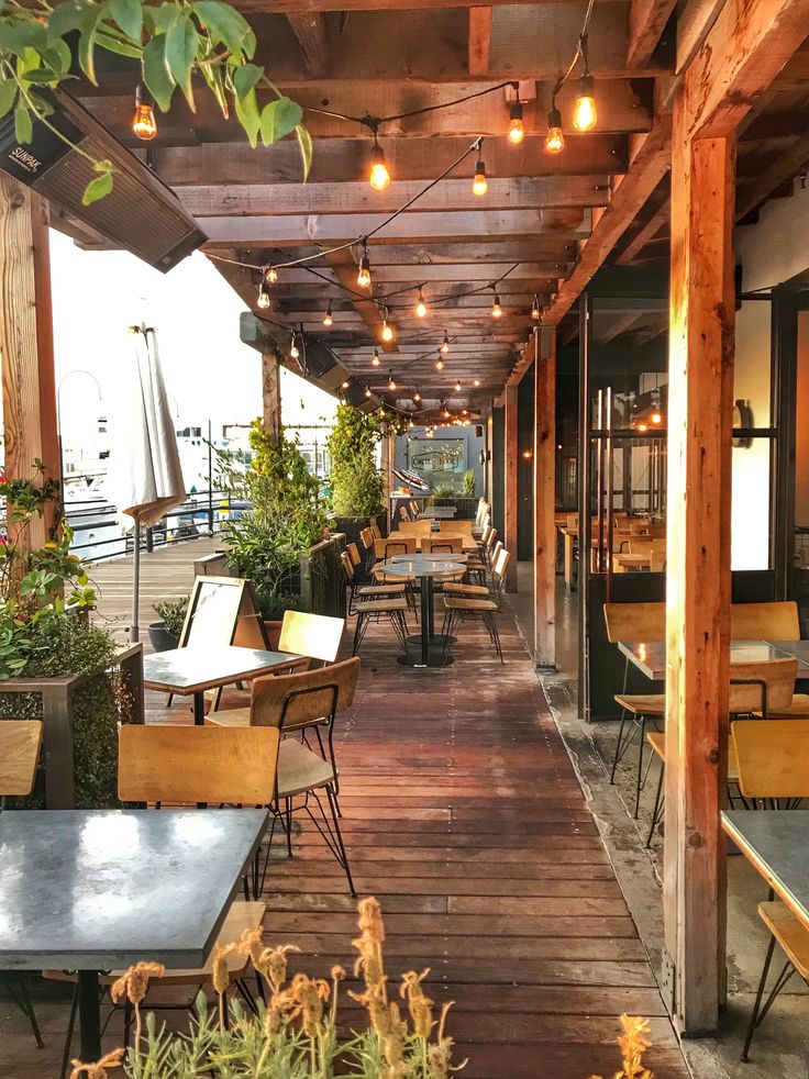 an outdoor seating area with tables and chairs on the deck, surrounded by potted plants