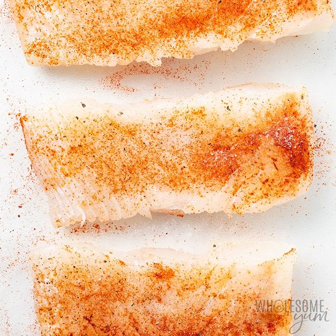 two fish fillets on a white surface covered in seasoning