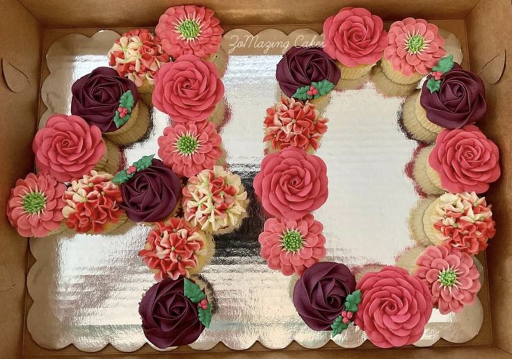 cupcakes decorated with pink and purple flowers in a cardboard box on a table