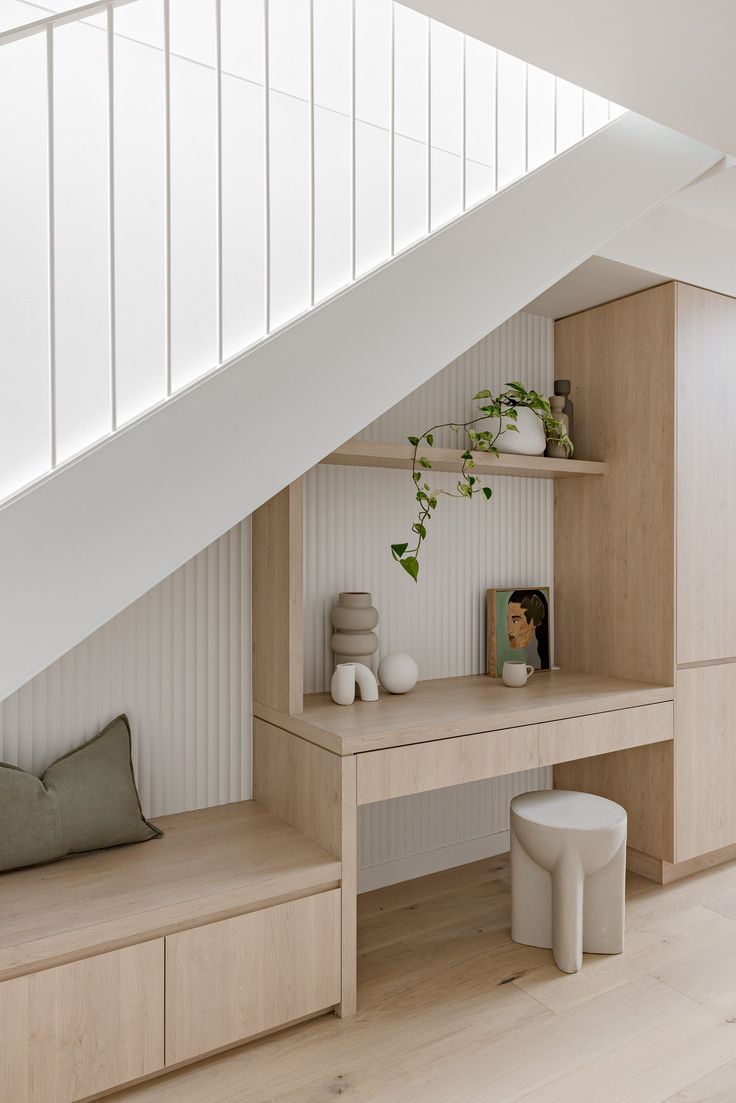 a wooden desk under the stairs in a room with white walls and wood flooring