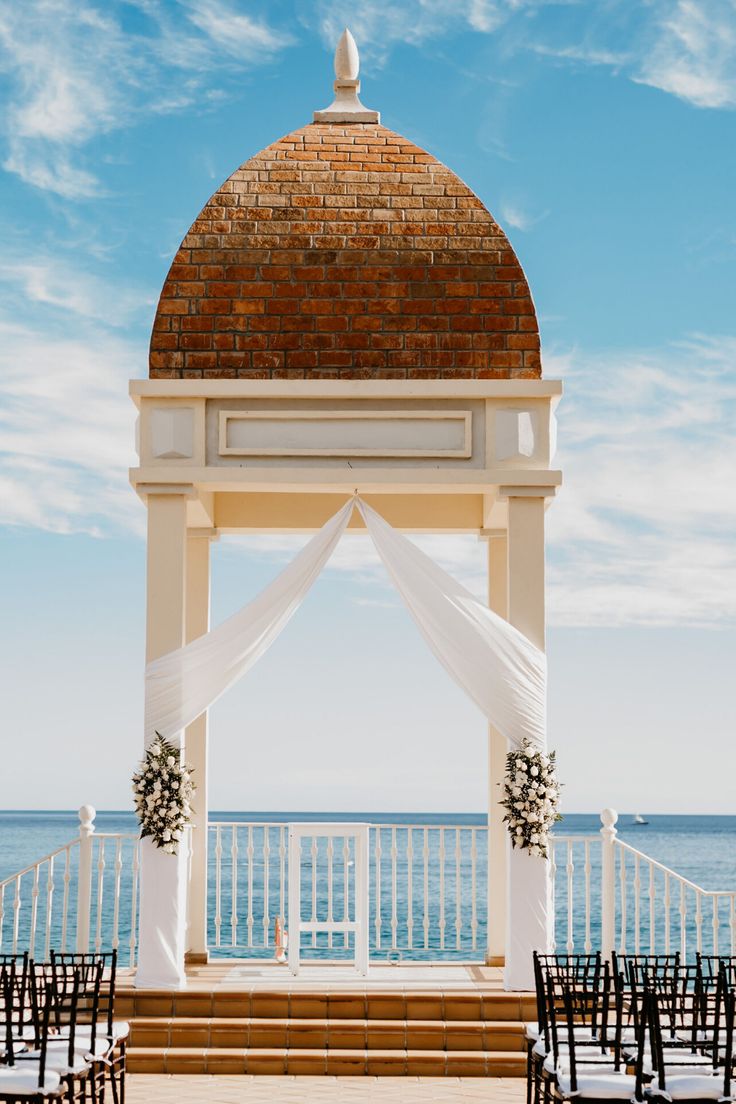 an outdoor wedding set up with chairs and a gazebo overlooking the ocean on a sunny day