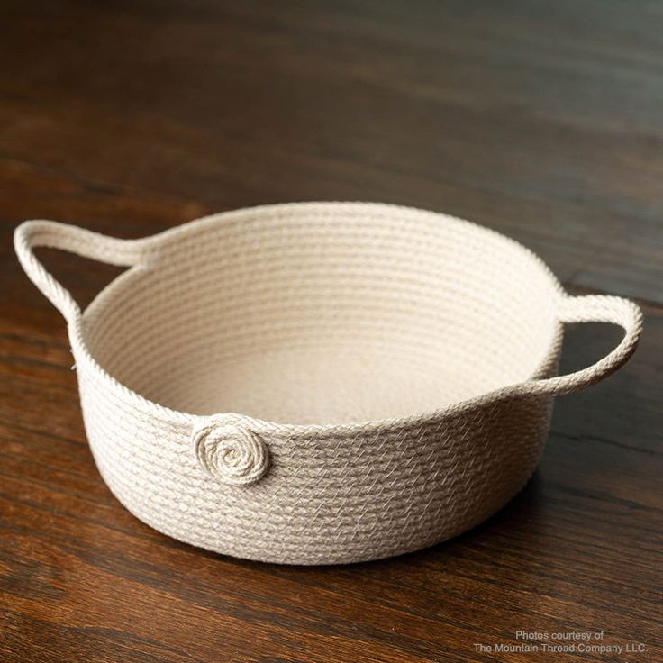 a white rope basket sitting on top of a wooden table next to a knife and fork