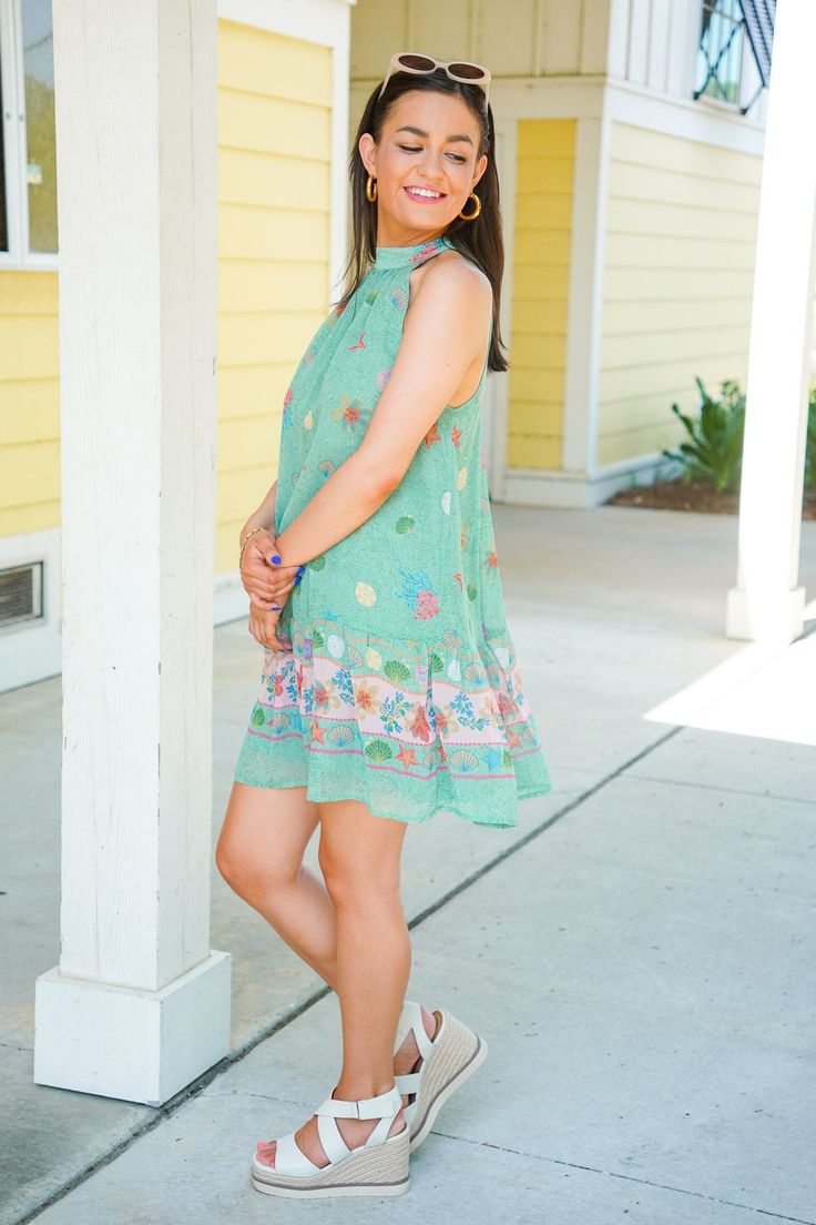 The Shelly Dress is perfect for a beach vacation or dinner by the ocean! This mini dress features a relaxed fit, sleeveless design, mock neckline with a self tie at the back, and a playful back cutout. The dress showcases a green hue with a beachy print of shells, starfish, and coral. Pair with our sunglasses and some sandals for a chic look! It is lightweight, fully lined, and fits true to size. 100% Polyester Brand- Olivaceous Model is 5'5" and is wearing a small Summer Sleeveless Mini Dress For Beach, Green Sleeveless Beach Dress For Spring, Green Mini Sleeveless Dress For Summer, Green Sleeveless Dress For Beach Vacation, Green Sleeveless Dress For Spring Beach Outing, Green Sleeveless Dress For Spring Beach Occasion, Casual Halter Neck Beach Dress For Summer Outings, Green Casual Sundress For Vacation, Summer Sleeveless Dress For Spring Beach Party