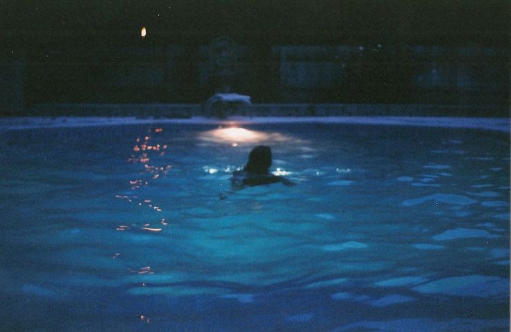 a person in a pool at night with their head turned to the side and lights on