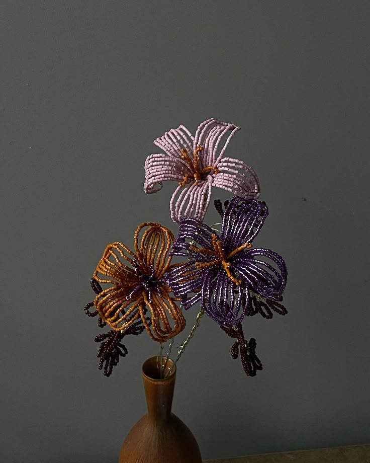 a vase filled with purple flowers on top of a wooden table next to a gray wall