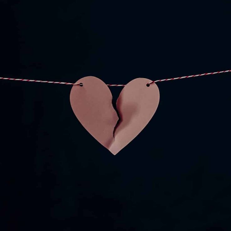 two paper hearts hanging on a rope with string attached to it, against a black background