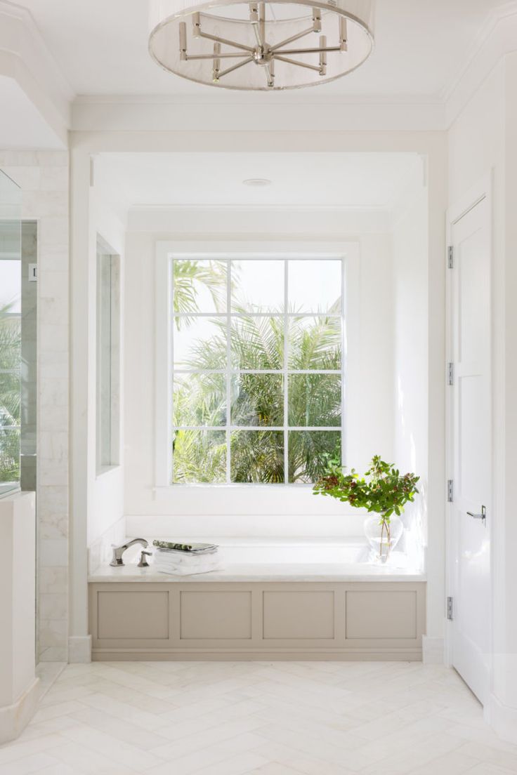 a white bathroom with a large window, tub and plant in the corner next to it