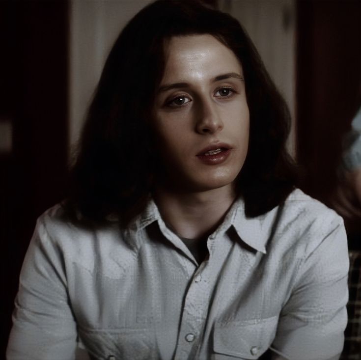 a woman with long hair wearing a white shirt and sitting in a chair looking at the camera