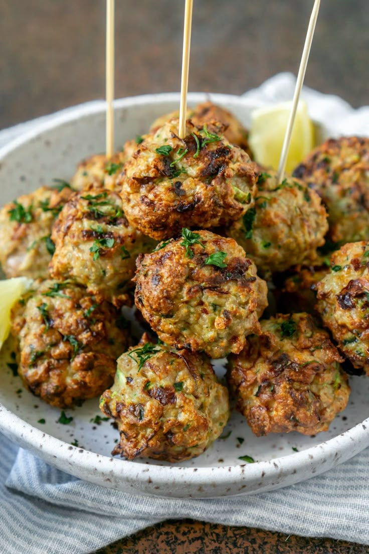 a white bowl filled with meatballs and toothpicks next to lemon wedges