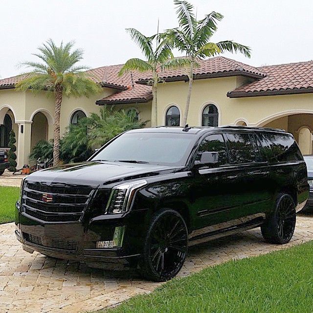 a black suv parked in front of a house with palm trees on the side of it