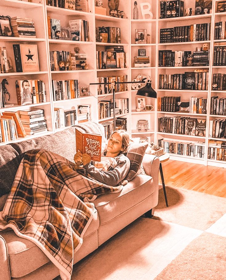 a person laying on a couch in front of a bookshelf with lots of books