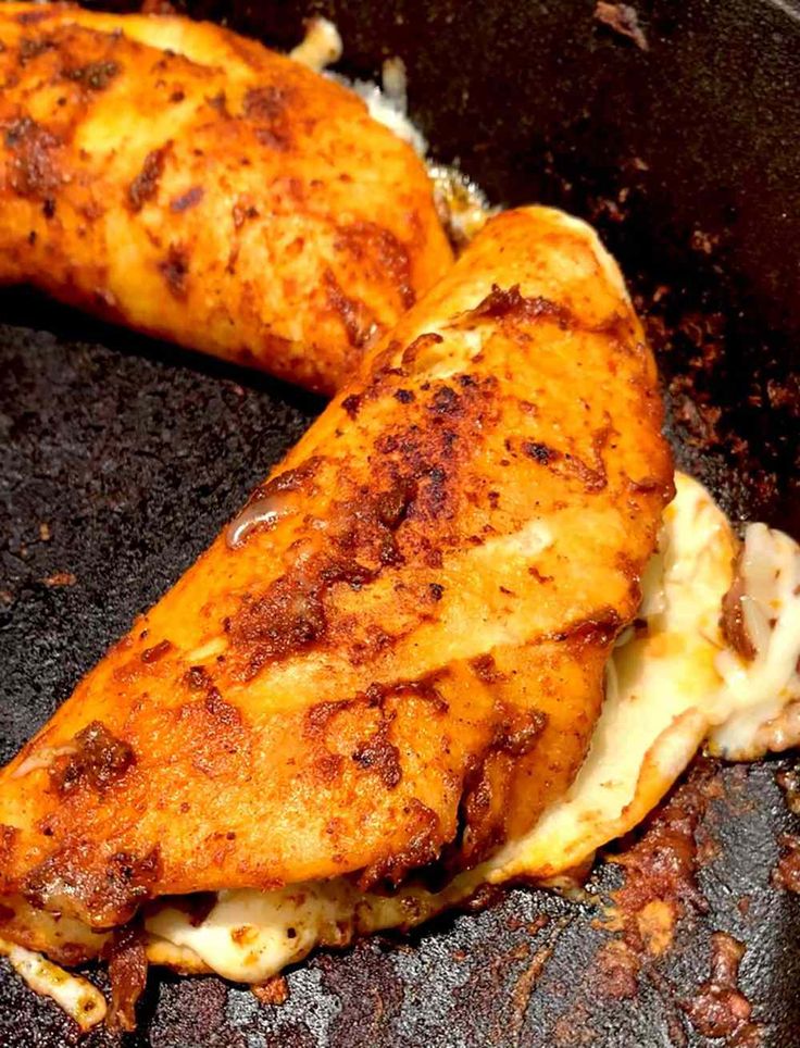 two pieces of chicken are cooking in a frying pan with melted cheese on top