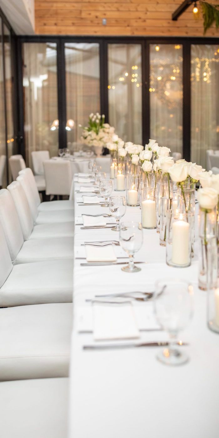 a long table is set with white flowers and candles for an elegant dinner or reception