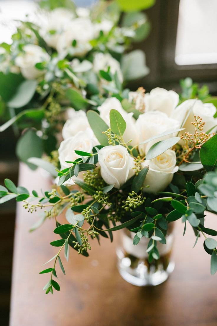 white roses and greenery in a vase on a table