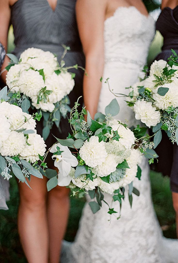 three bridesmaids holding bouquets of white flowers and greenery in their hands