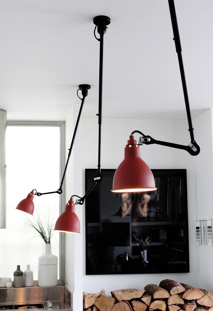 two red lamps hanging from the ceiling in a room with wood stacked on the floor