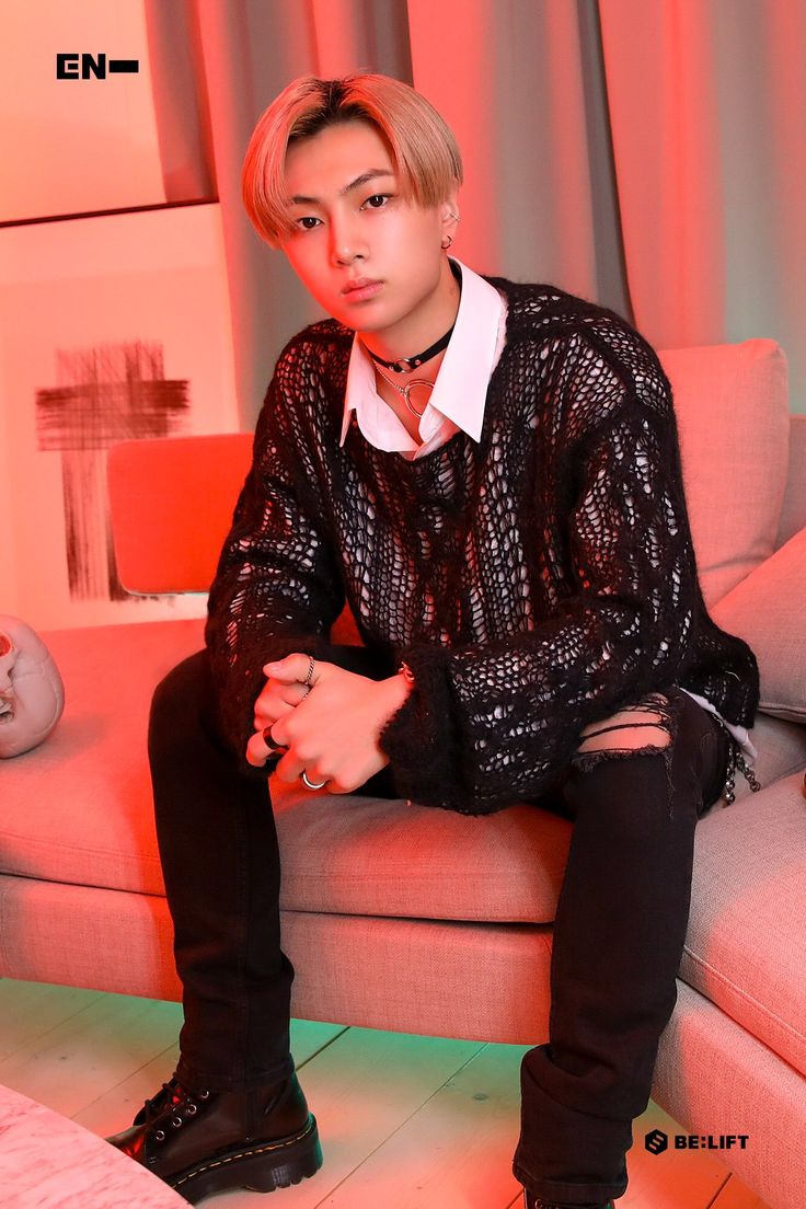 a young man sitting on top of a couch next to a pink light in a living room