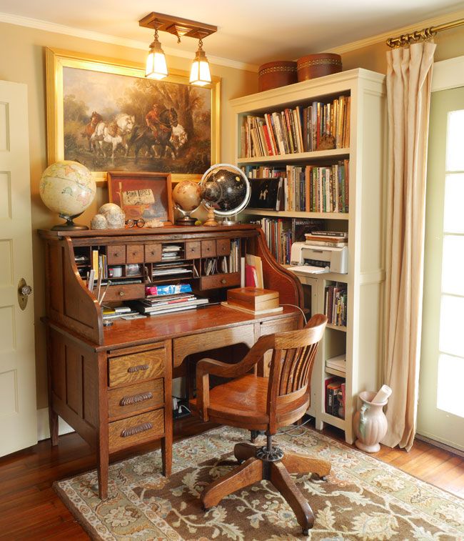 an old fashioned desk in the corner of a room with bookshelves and paintings on the wall