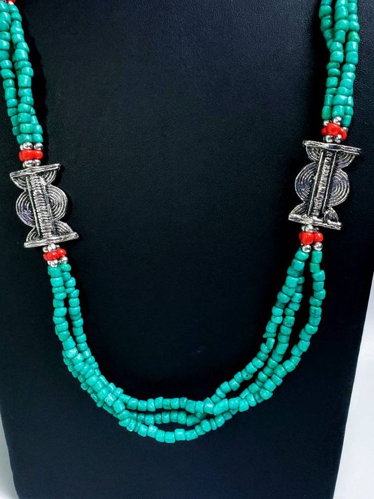 Add color and pizzazz to any outfit with this beautiful hand crafted Tibetan turquoise color multi strand bead necklace with silver tone amulets. The red faux coral makes the amulets pop! A simple but very striking necklace! Can be worn day or night. Makes a beautiful gift! Twist the necklace for a totally different look! Excellent quality and craftsmanship. - 3 strands of irregular beads - bright turquoise/teal color - silvertone amulets - secure hook closure Shop more necklaces: https://www.et Handmade Turquoise Beaded Necklace For Festivals, Turquoise Necklaces With Colorful Beads For Festivals, Festival Turquoise Beaded Necklaces, Handmade Spiritual Multi-strand Turquoise Necklace, Traditional Multi-strand Turquoise Beaded Necklace, Traditional Turquoise Multi-strand Beaded Necklace, Hand-strung Turquoise Jewelry For Festivals, Traditional Multi-strand Turquoise Necklace, Bohemian Turquoise Beads For Festivals