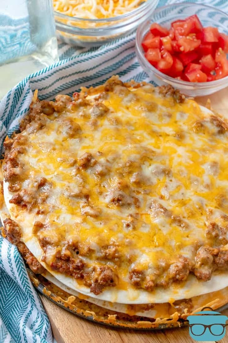 a pizza sitting on top of a wooden cutting board next to a bowl of tomatoes