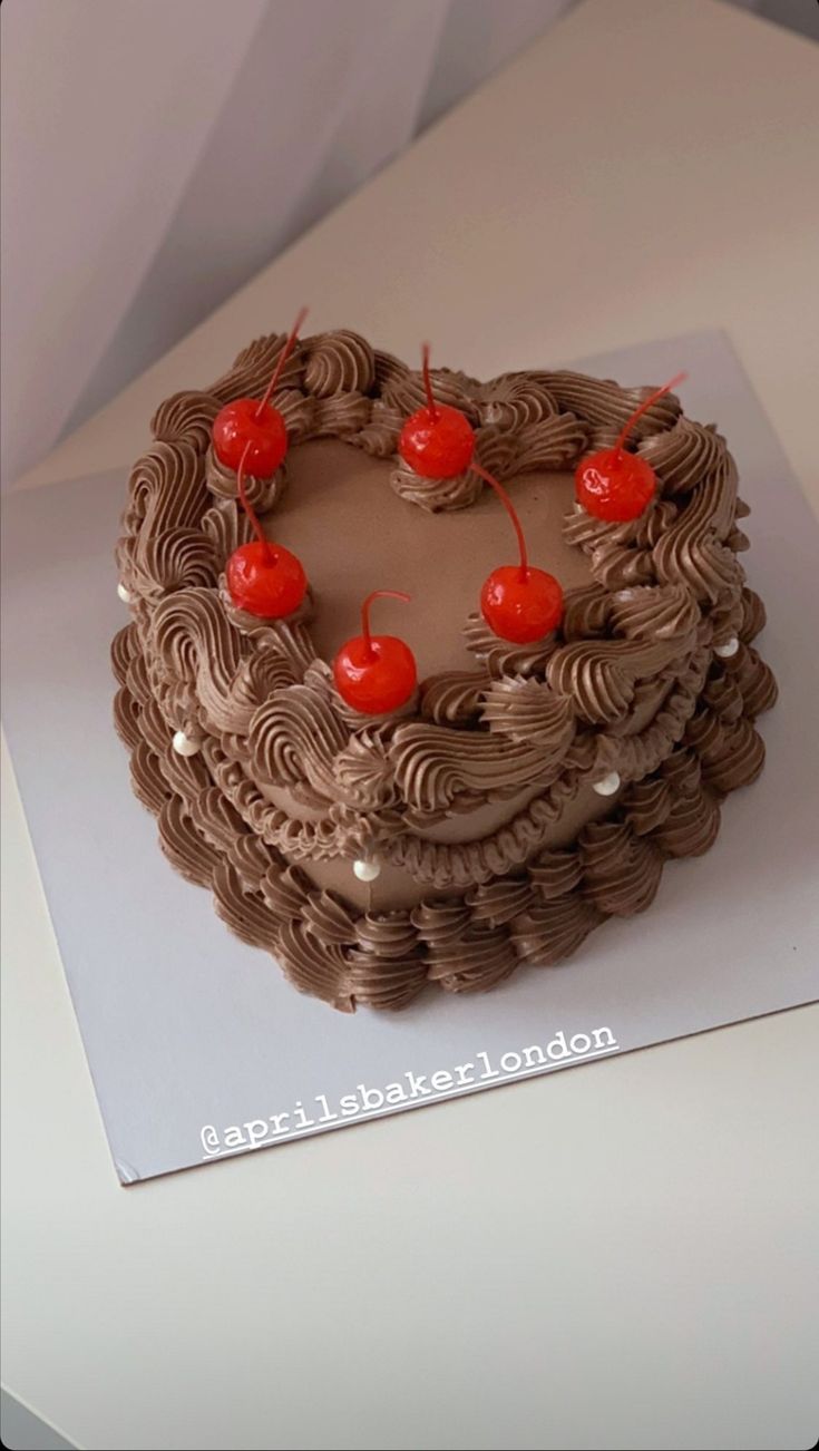 a heart - shaped chocolate cake with cherries on top sits on a white table