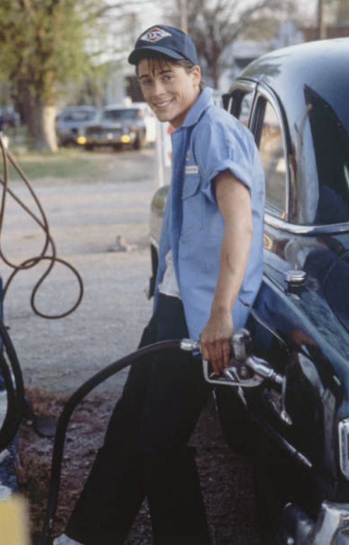 a man in blue shirt and cap filling gas into car at gas pump with hose