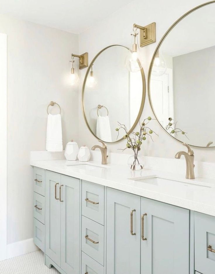 a bathroom with two round mirrors above the sinks and blue cabinetry, along with white towels